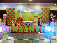 Birthday stage setup with a Barnyard banner, Shaped foil balloons of a Cow and Pig on pillars and a picket fence on the stage front along with the baby name in large alphabet cutouts.