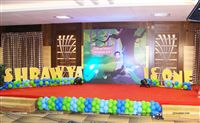Backdrop on the stage with a caricature of the birthday girl and peacocks in a jungle scene. Alphabet blocks with the babys name on either side of the backdrop and a string of balloons at the base