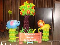 Jungle photo booth completely made with balloons that includes a fruiting tree, a Lion & Elephant foil balloon on a green balloon pillar along with a cutout that contains the little ones name. 